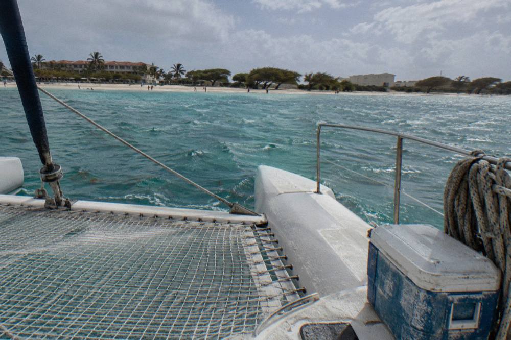 Wide catamaran deck with nets and railings gliding across calm turquoise water near the Aruba coast