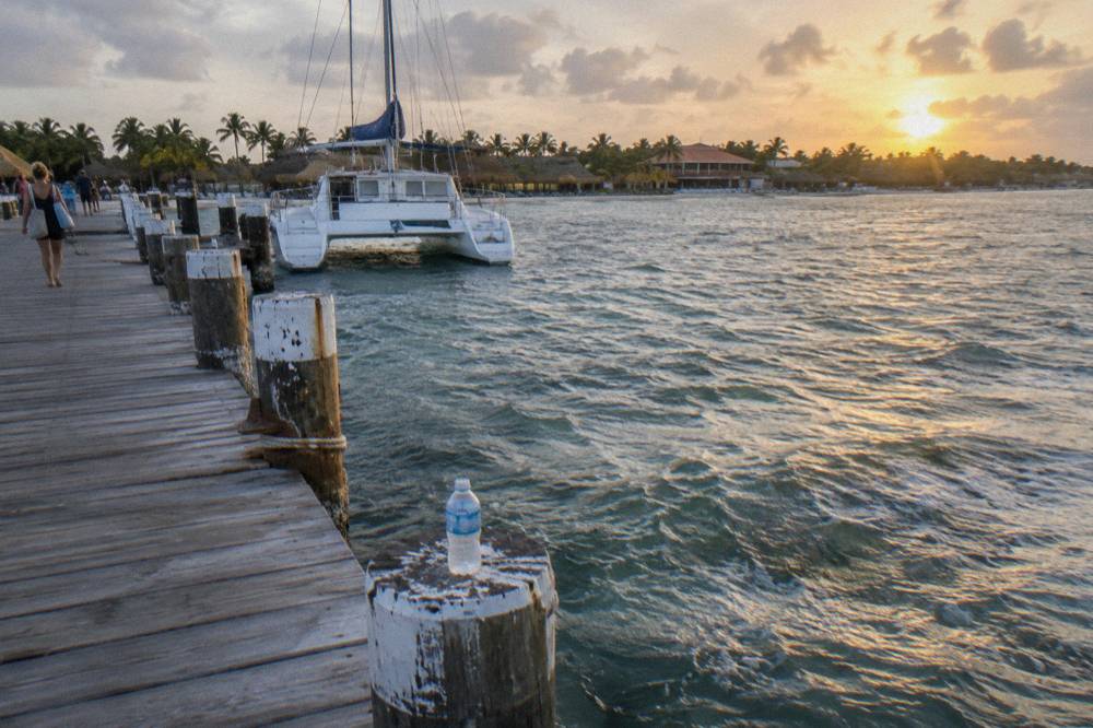 Wooden pier extending into calm sea toward a moored catamaran at golden hour on Palm Beach