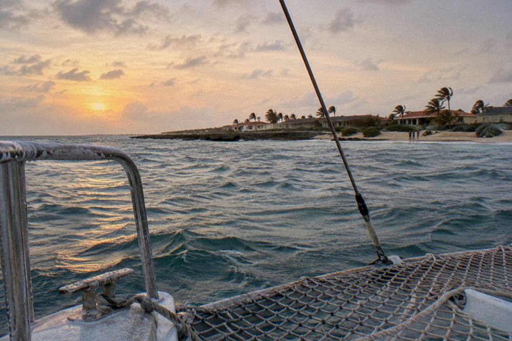 Catamaran nets and railing with calm sea and orange sky as daylight fades