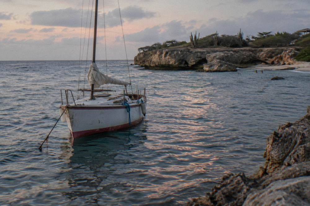 A small sailing boat anchored near shore with calm water reflecting pink light