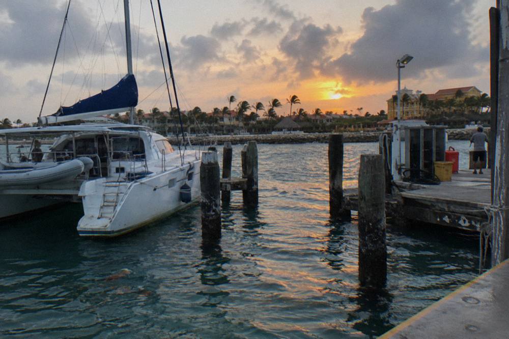 White catamaran moored beside a wooden pier on a calm sea at dusk
