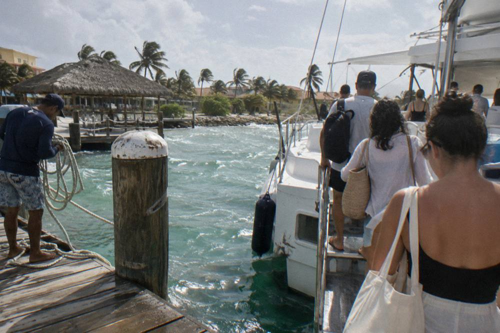 Guests boarding a catamaran at a wooden pier while crew holds a rope