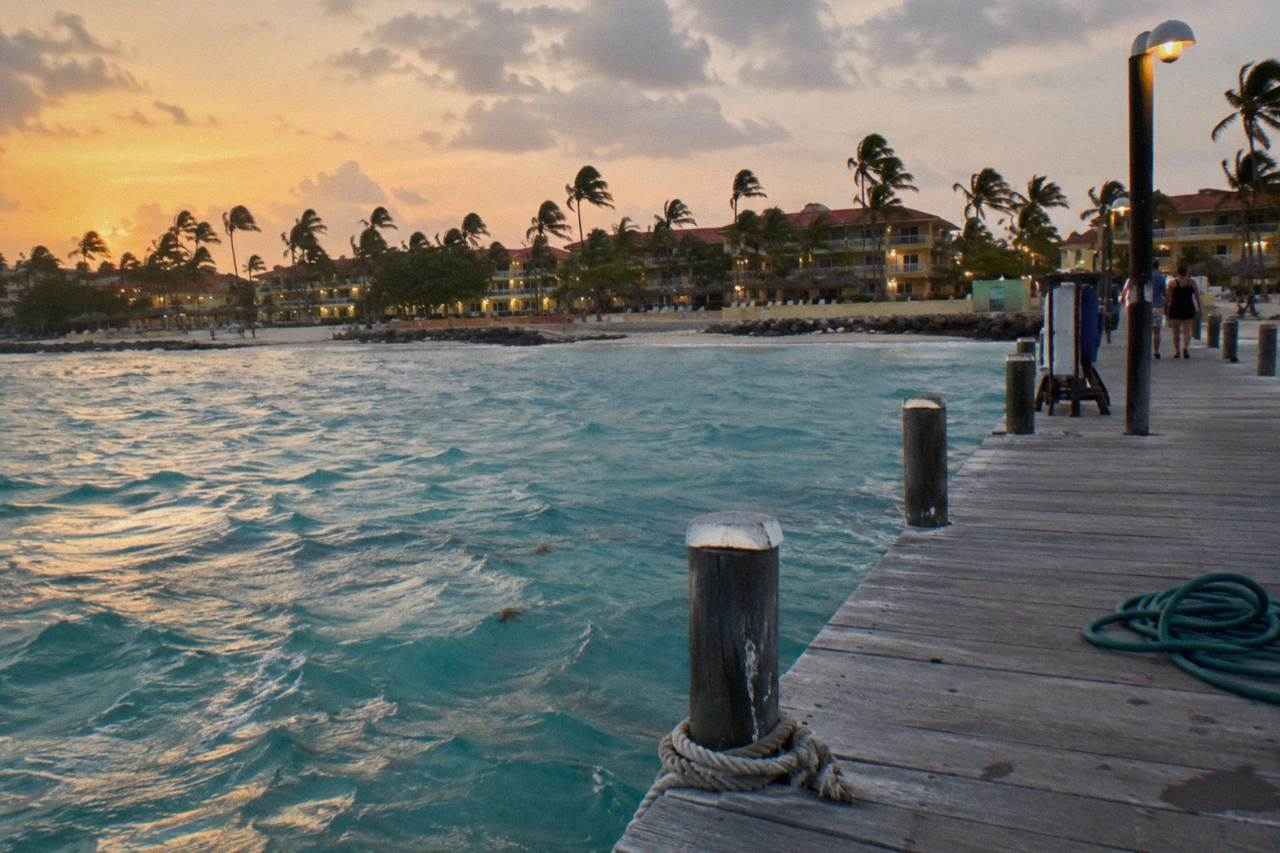 Wooden pier extending over calm turquoise water toward an orange evening sky