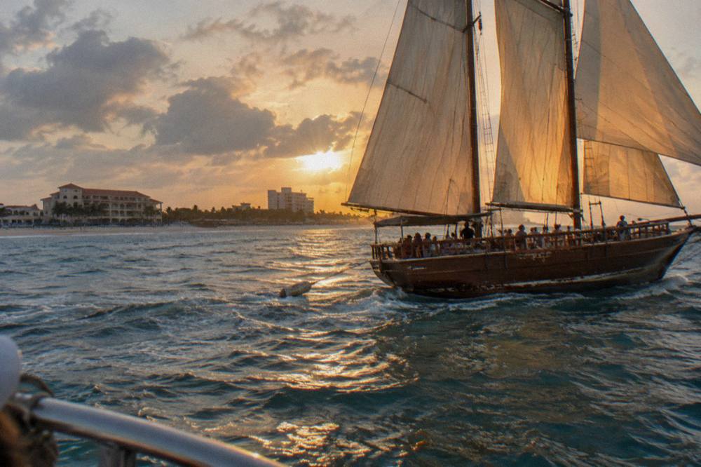 A wooden pirate-style schooner under sail off the Aruba coast as the sky turns orange
