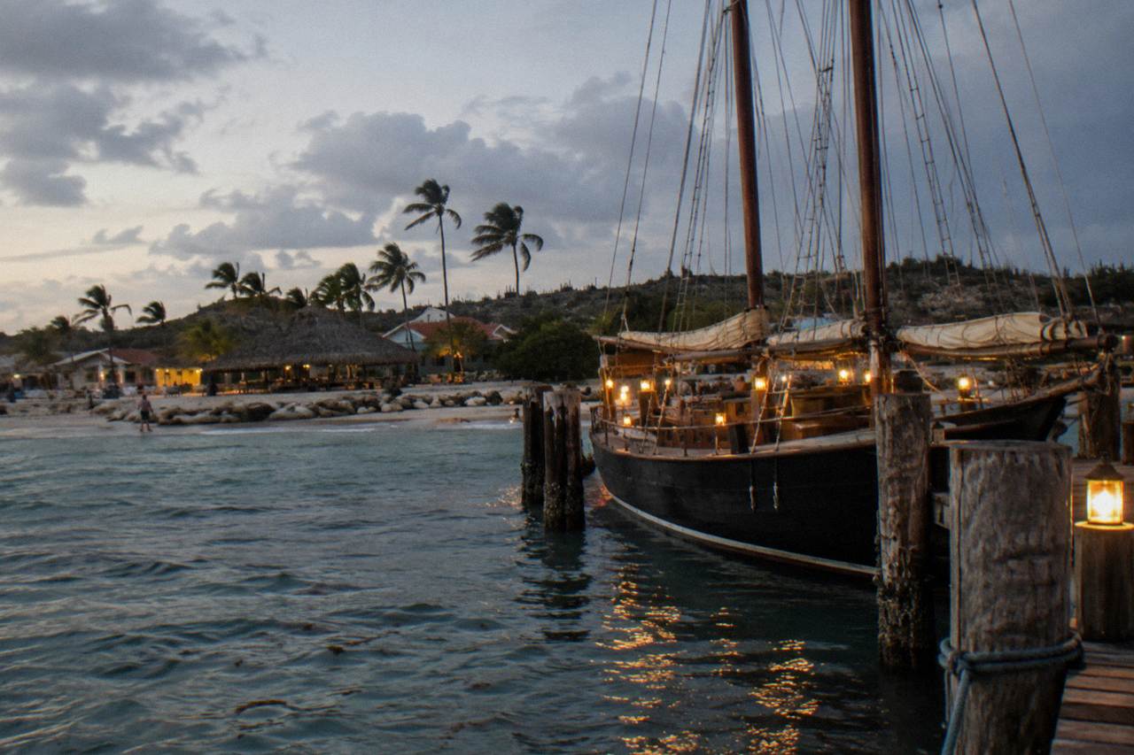 A pirate-style schooner with tall masts moored beside a Palm Beach pier at dusk