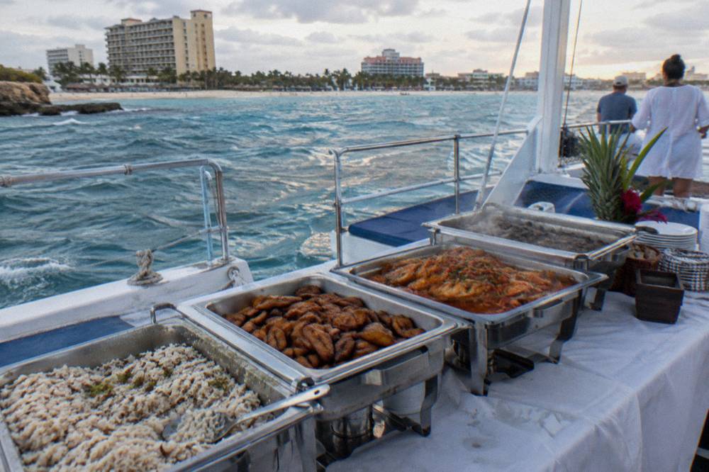 Buffet table of Caribbean dinner dishes set out on a boat deck at dusk