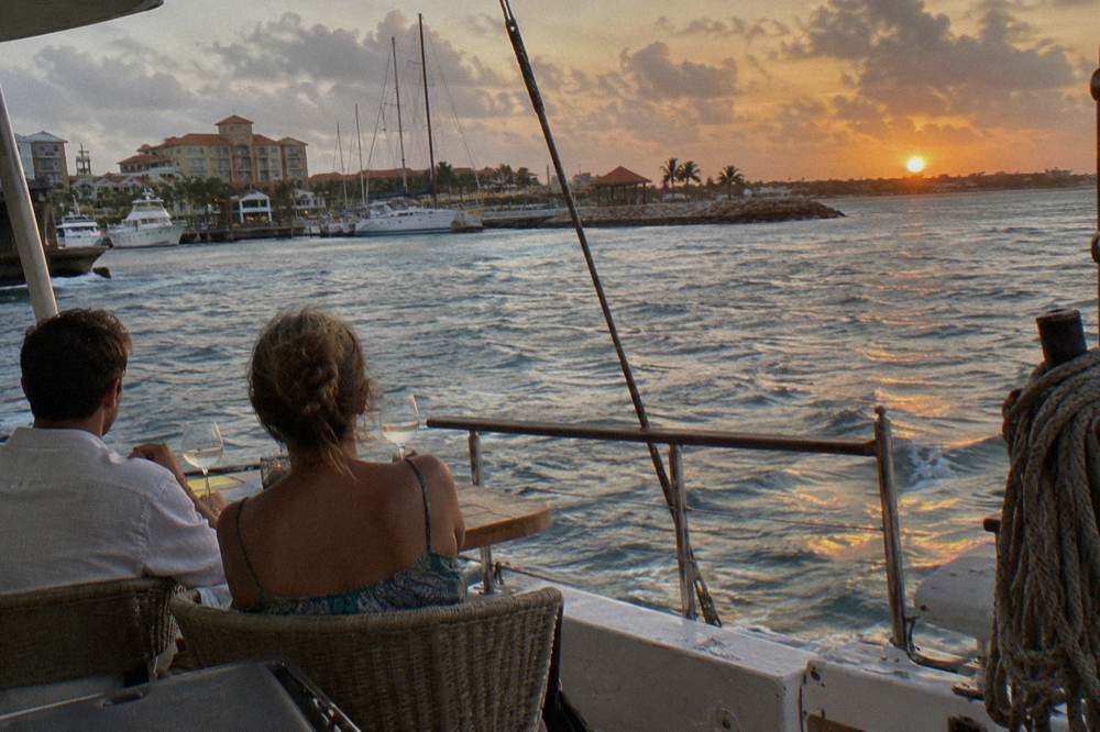 Couple at a dinner table on a boat deck watching the sun set over calm Caribbean water