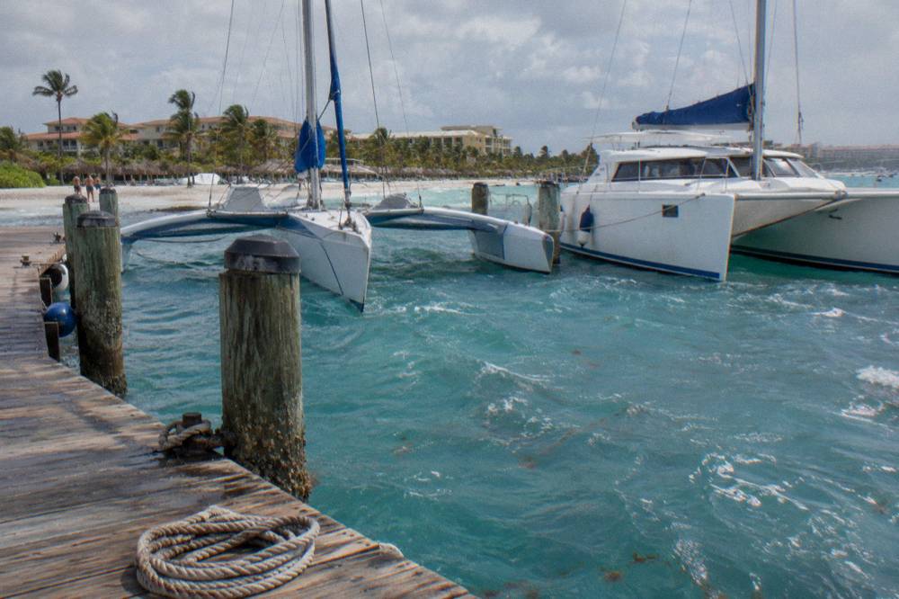 Trimaran and catamaran moored at a beach pier in late afternoon light along the Aruba coast