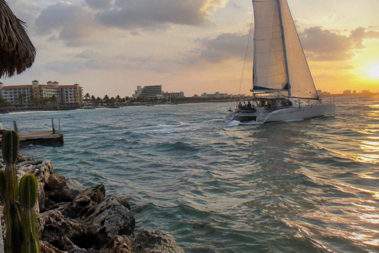 Catamaran under sail off the Aruba coast at sunset with calm sea and orange sky