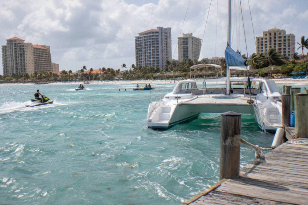 A white catamaran moored near a beach pier under a partly cloudy sky