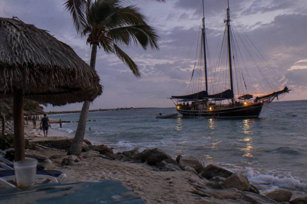Pirate style schooner with dark sails moored near a beach at dusk