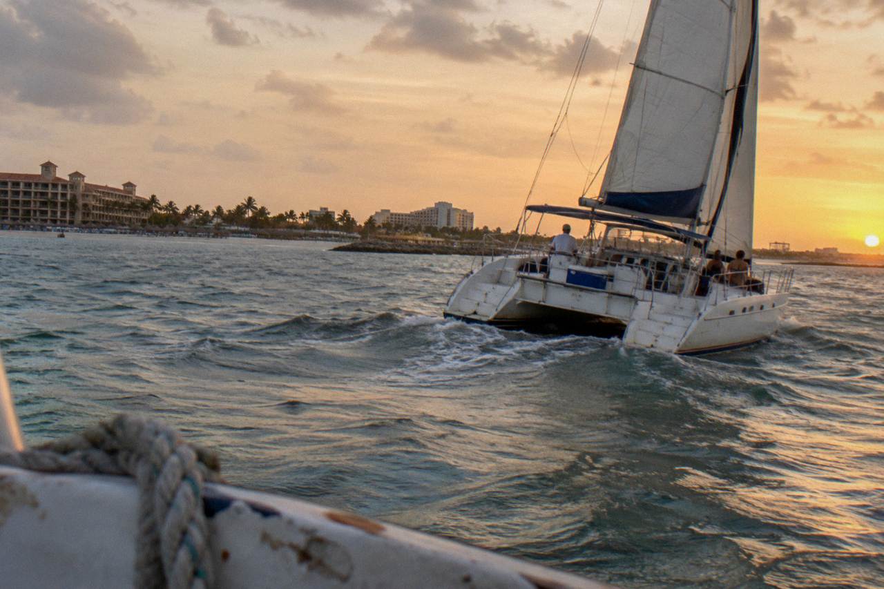 Catamaran with sails up cruising calm Caribbean water near Palm Beach at golden hour