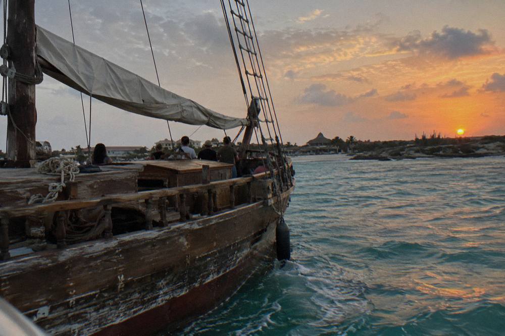 Wooden pirate schooner under sail on calm Caribbean water near Aruba at dusk