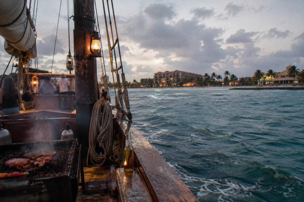 Evening view of a pirate schooner deck lit warm against a darkening sky over the Caribbean