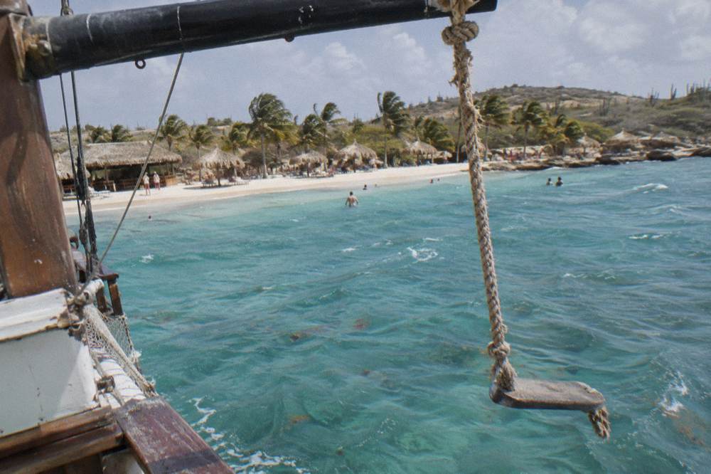 Rope swing hanging from the yardarm of a wooden schooner over clear turquoise water
