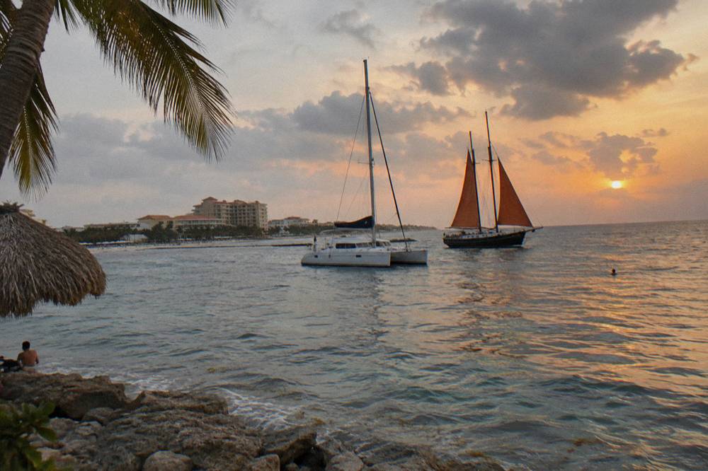 Catamaran and schooner sails anchored near each other off a Caribbean beach at sunset