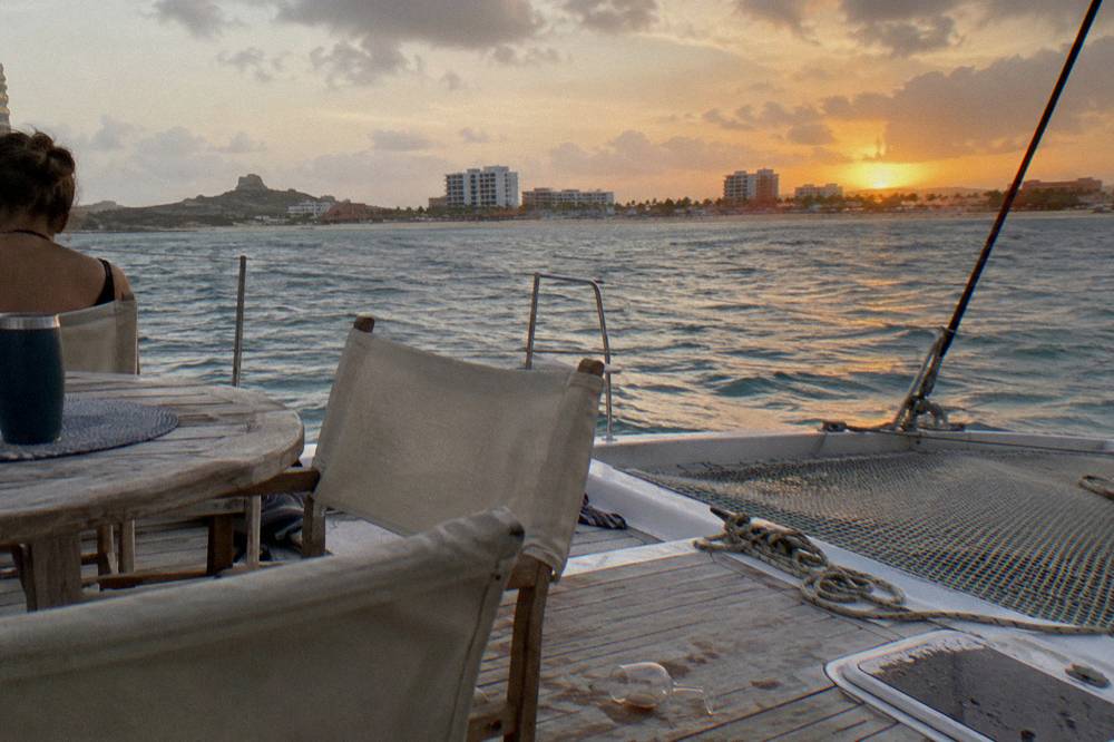 A group of chairs and a table set on the deck of a boat facing an orange evening horizon