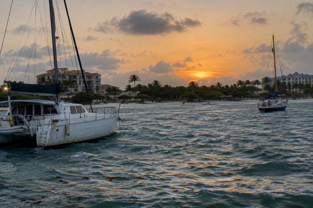 A catamaran and a sailing boat at anchor near the Palm Beach coastline under a fading orange sky