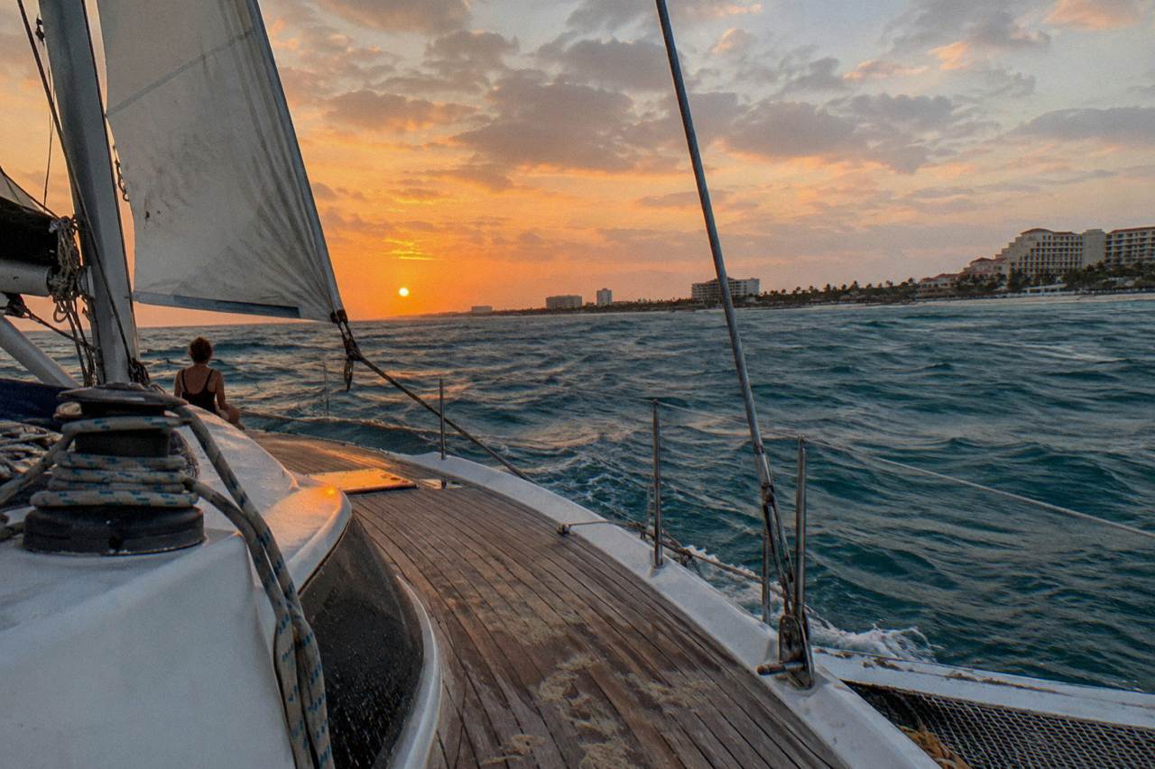 A private catamaran under sail off the Aruba coast as the sky turns orange over calm water