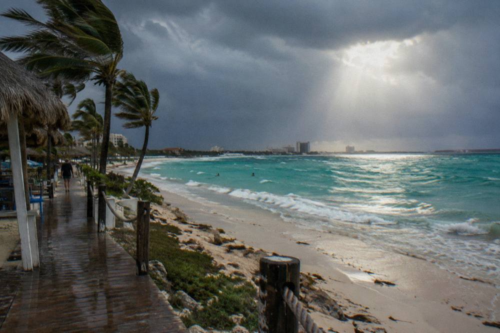 Palm Beach shoreline under dark rain clouds with sunlight breaking through over calm water