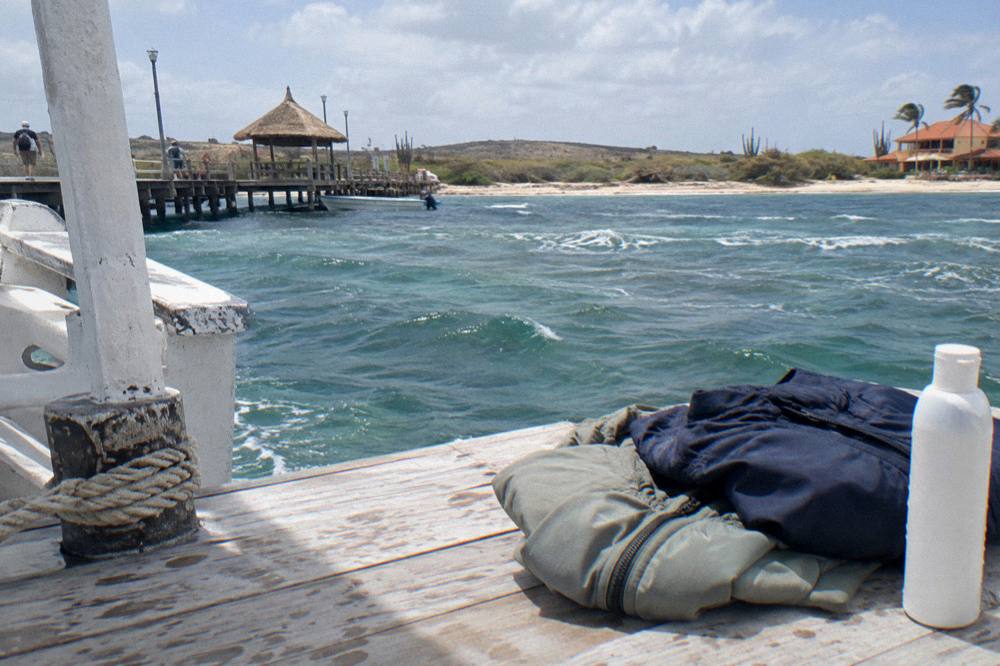 Folded light jackets and a mineral sunscreen bottle resting on a wooden boat deck before departure