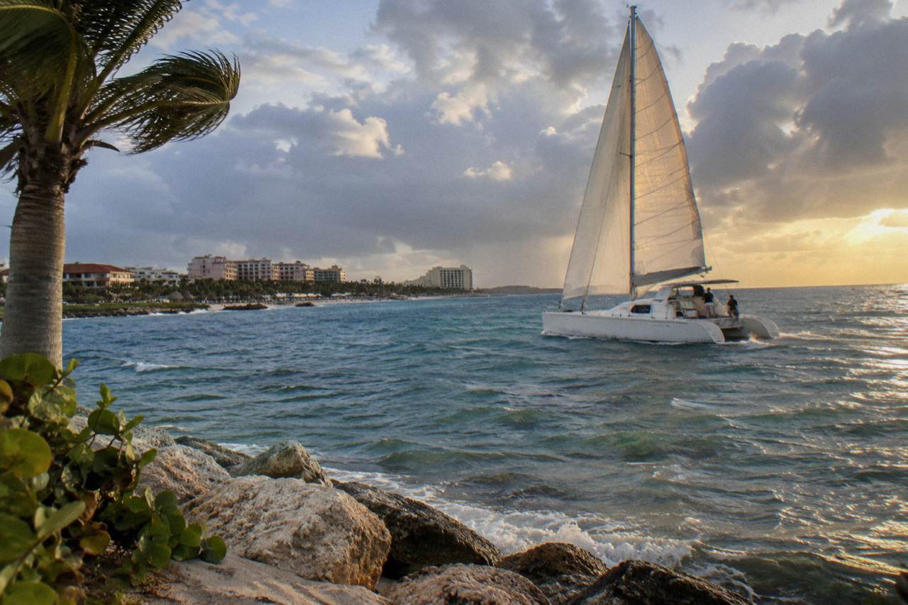 White catamaran sails across calm Caribbean water near Aruba under a partly cloudy evening sky