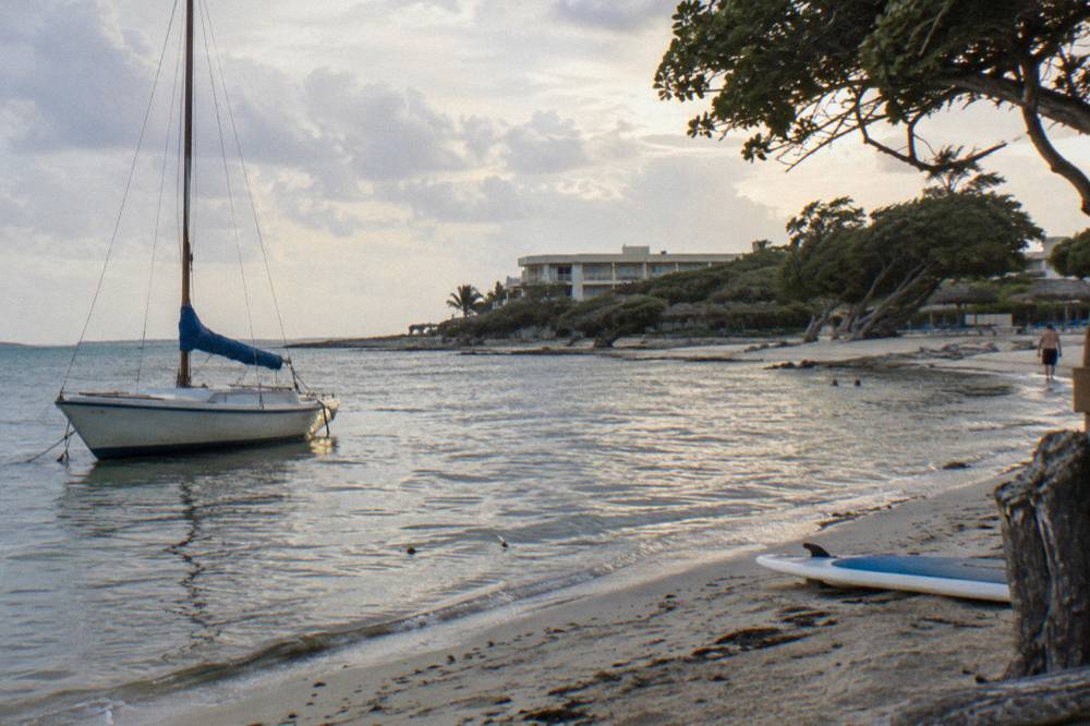 A small sailing boat anchored near shore with still water reflecting a pale evening sky