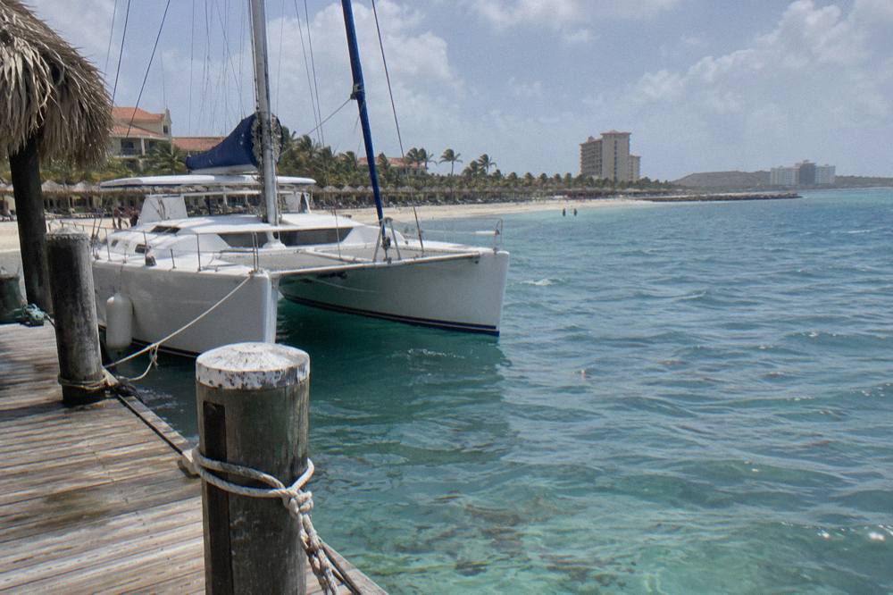 A catamaran moored in calm blue water beside a wooden pier on Palm Beach in Aruba