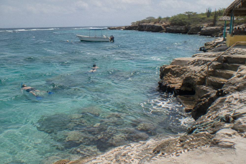 Snorkelers floating above a shallow reef in clear water with a boat anchored nearby