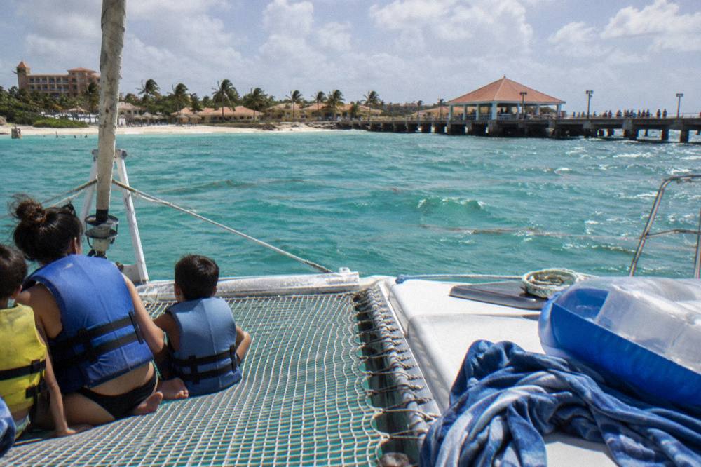 A family seated on a catamaran net beside a pier over turquoise water