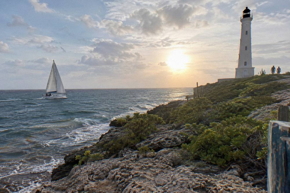 A sailboat under way along the coast as the late afternoon sun lowers over the sea