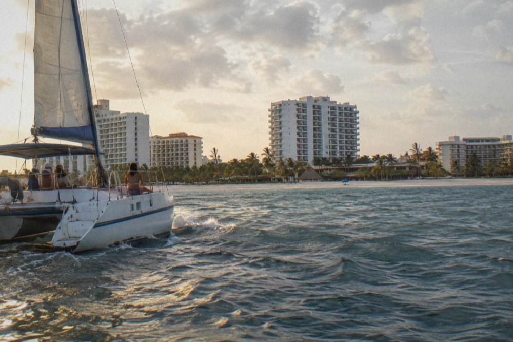 An open deck catamaran crossing golden water with resort towers along the shoreline behind it