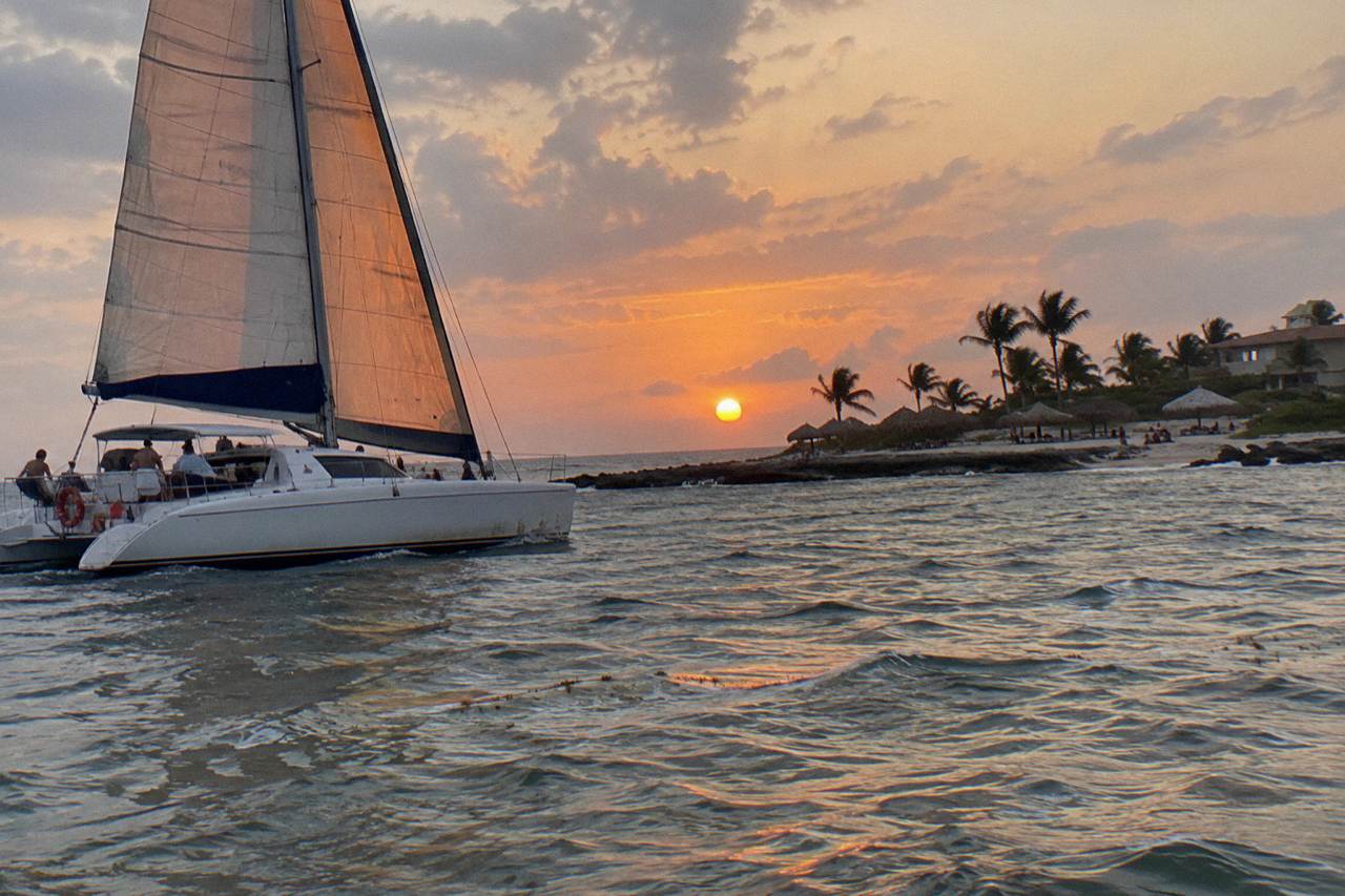 A catamaran under sail on calm Caribbean water off Aruba at dusk