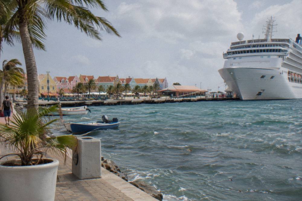 A cruise ship docked at the terminal in Oranjestad with small boats in the harbor