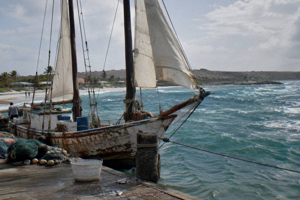 A wooden schooner moored at a Caribbean pier with sails up in daylight