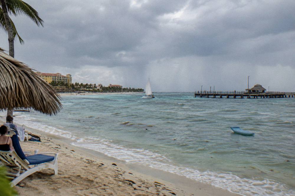 A darkening sky over calm Caribbean water with a sailboat heading toward shore