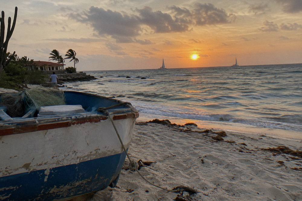 Orange sunset over calm Caribbean water with sailboats silhouetted near the Aruban coastline