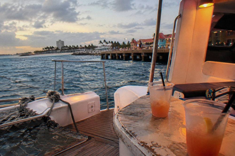 Open-air catamaran deck with drinks on a table and calm sea beyond at dusk