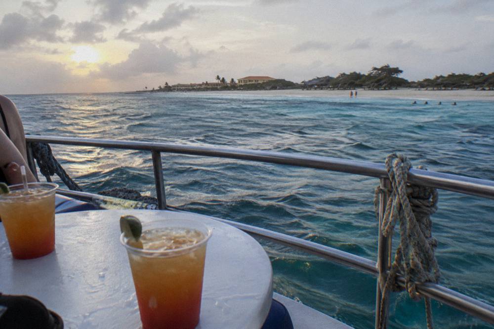 A table for two with drinks on a boat rail with the sun low over open water