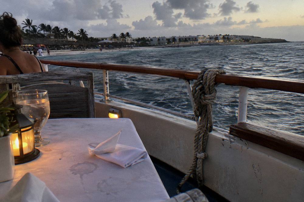 A boat deck lit by warm lantern light with the dark sea beyond at dusk