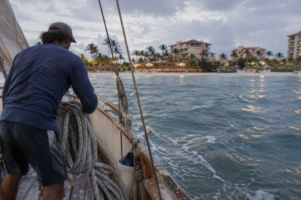 Crew member coiling a rope on the deck of a wooden sailing boat at dusk