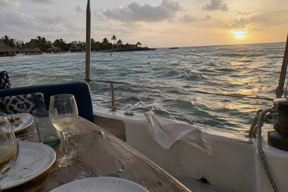 Dinner table set with glasses and plates on the deck of a boat at sunset