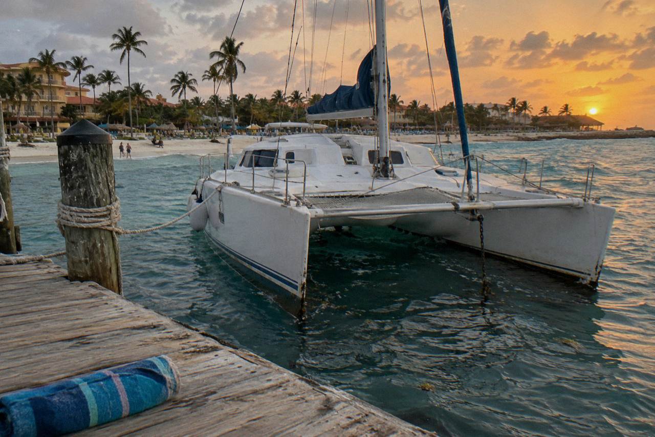Sunset catamaran moored at a wooden pier on Palm Beach with calm water and an orange sky