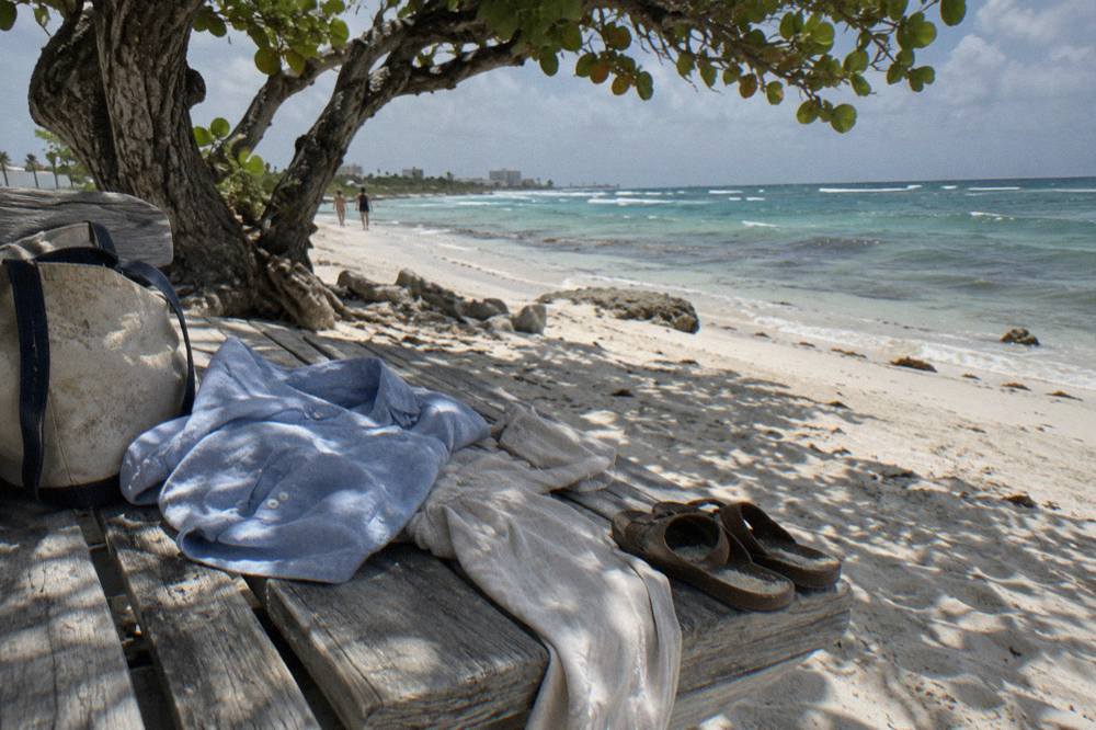 Folded light clothing and sandals laid out on a wooden bench beside a tote bag