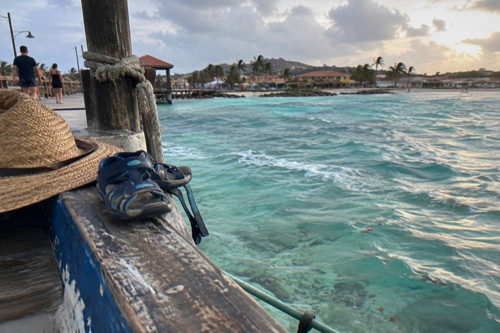 Pair of sandals and a straw hat resting on the edge of a wooden boat deck at dusk