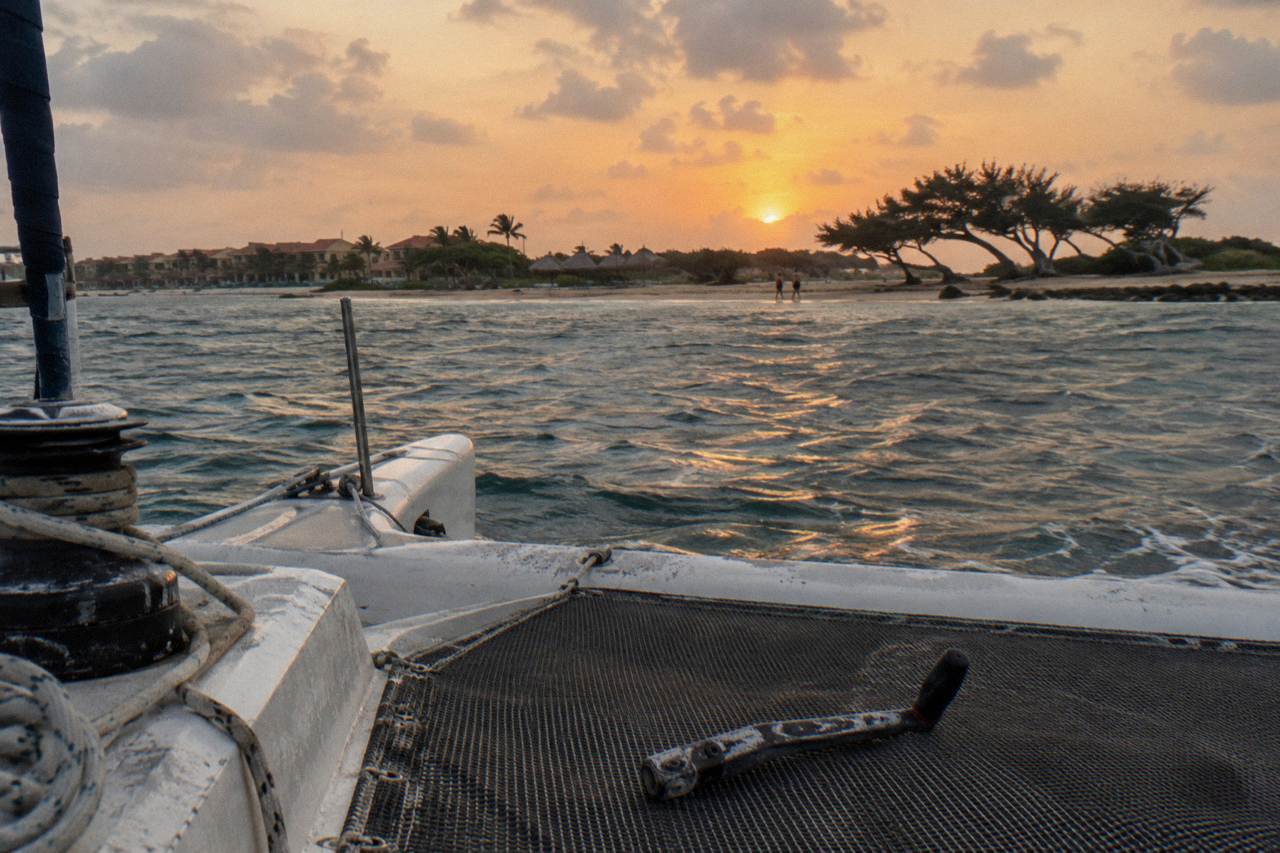 Open catamaran deck at dusk with calm sea and orange sky over the Aruba coastline